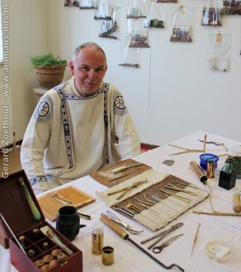 Een als Romeinse arts geklede volwassene zit achter een tafel met gereconstrueerde medische instrumenten.